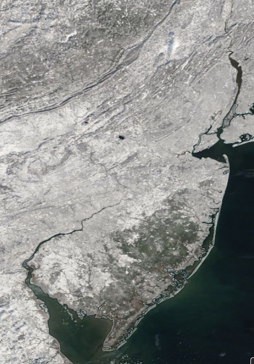Figure 6. NASA MODIS visible satellite image on the morning of January 20th showing snow cover over New Jersey and surrounding states. The dark spot in west central NJ is unfrozen Round Valley Reservoir (Hunterdon) and the dark area in south Jersey is the Pinelands, where the coniferous trees “hide” the underlying snow cover from the satellite view. The far southeast had a thin cover, thus the tan hue in spots. NJ skies are cloud-free with a small area of clouds lying just north of Sussex County over Orange County, NY. NASA MODIS visible satellite image on the morning of January 20th showing snow cover over New Jersey and surrounding states.